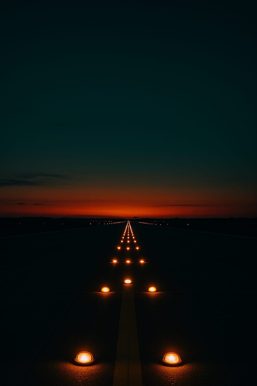 Runway lights leading towards a warm horizon at dusk